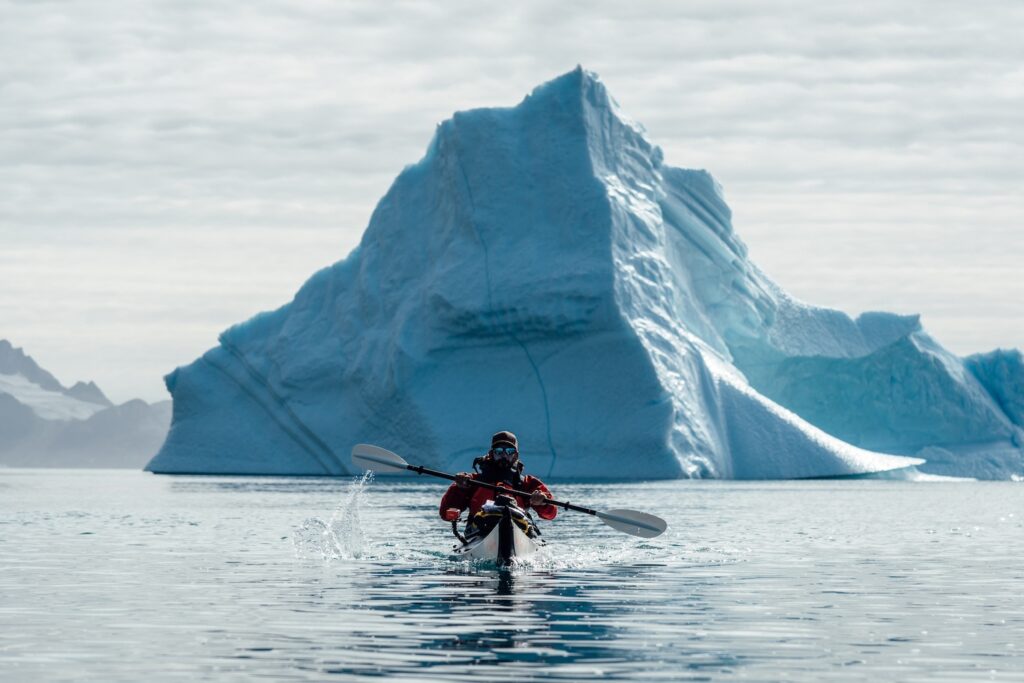 A-kayaker-paddles-with-a-large-iceberg-directly-behind-him-Just-North-Of-Kuummiut Groenlândia
