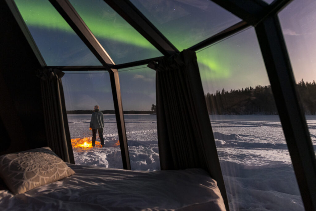 Person admiring northern lights outside the glass igloo