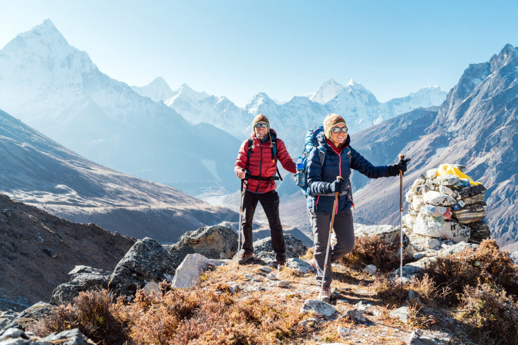 Couple following Everest Base Camp trekking route near Dughla 4620m. Backpackers carrying Backpacks and using trekking poles and enjoying valley view with Ama Dablam 6812m peak