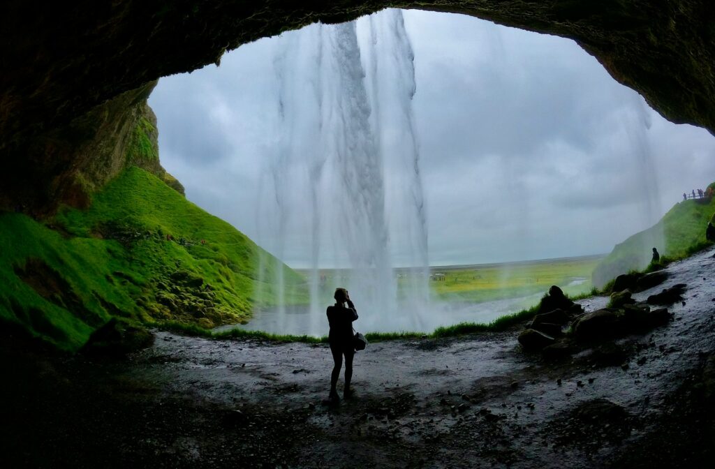 Mulher fotografando por trás da Seljalandsfoss na Islândia